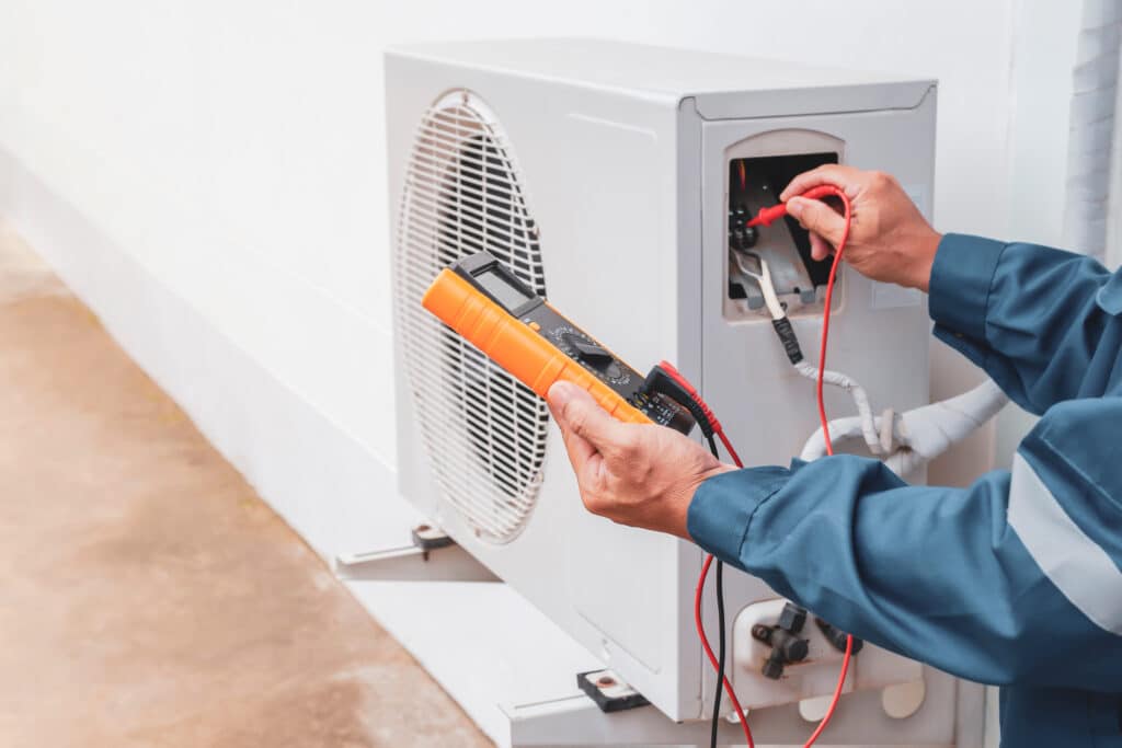 Un électricien effectuant des tests sur une pompe à chaleur extérieure pour un système de chauffage et climatisation.