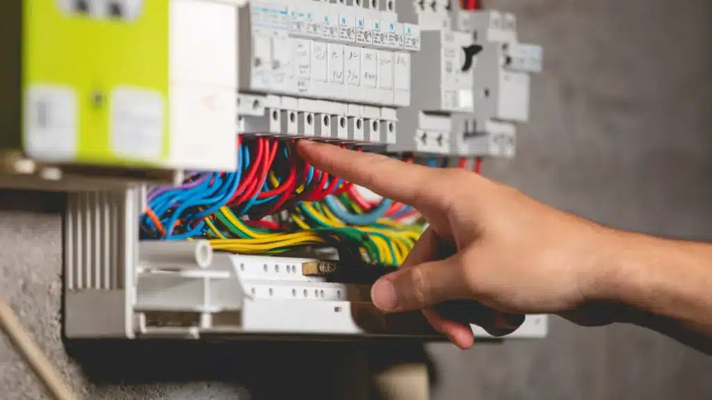 Un doigt pointant des câbles dans un tableau électrique lors de la recherche d'une panne électrique.